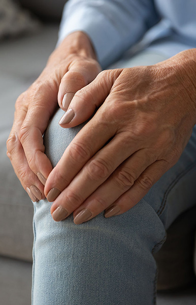 Close up older woman massaging touching knee with hands, feeling pain, mature female suffering from ache in leg, sitting on couch at home, feeling unwell, health problem concept, osteoarthritis